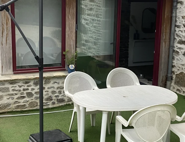 Terrasse du gîte en Bretagne avec table et chaises de jardin blanches sous un grand parasol, idéale pour profiter des repas en extérieur
