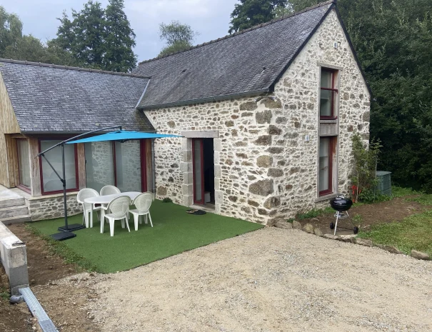 Gîte en pierre typique de Bretagne avec terrasse équipée de table, chaises et parasol, situé à Beaussais-sur-Mer, idéal pour des vacances en famille.